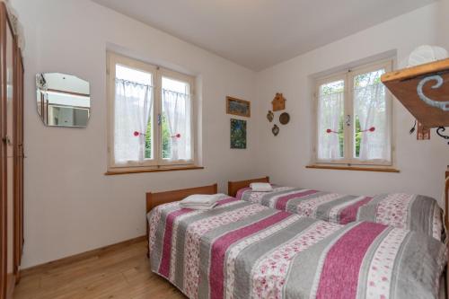 two beds in a bedroom with white walls and windows at Villa Elisena in Falcade