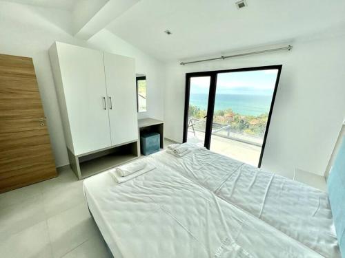 a white bedroom with a large bed and a large window at Villa Balchik in Balchik