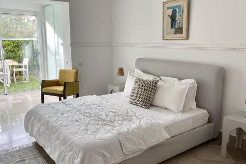 ein Schlafzimmer mit einem weißen Bett mit einem Stuhl und einem Fenster in der Unterkunft Sindbad House in La Marsa