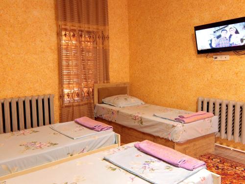 Habitación con 2 camas y TV en la pared. en LION Guest House, en Bukhara