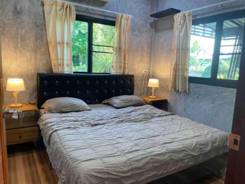 a bedroom with a bed with two lamps and two windows at Ban Aob Maiy(บ้านโอบไม้) in Ban Si Wicha