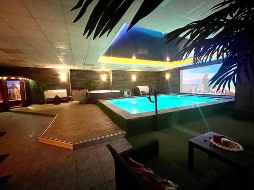 a large swimming pool in a building with a tv at COCOONING SPA - Gîte avec piscine, jacuzzi, sauna in Marck