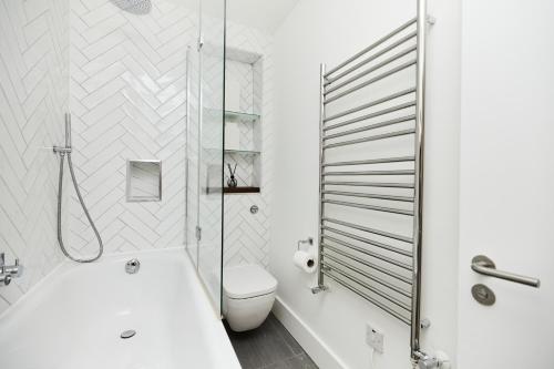 a bathroom with a white tub and a toilet at The Ravenscourt Park Escape - Bright 2BDR Flat in London