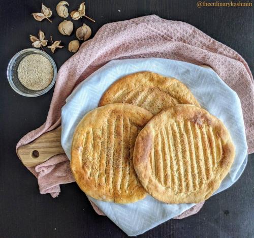 dois pães sentados em cima de um prato com uma colher de madeira em Taj Mahal Residency Muzaffarabad em Muzaffarabad