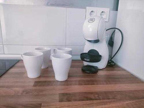 a coffee maker sitting on the floor next to four cups at San Centro Airport IFEMA Wizink Metropolitano Apartments in Madrid