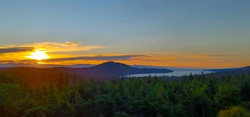 a sunset over a forested area with a mountain in the background at Gorgeous Private Estate With Ocean and Mountain View in Nanoose Bay