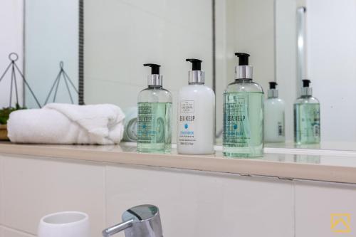 a shelf with four bottles of soap and towels at Luxury 2-bed In central MK By Valore Property Services in Milton Keynes