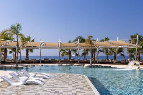 a swimming pool with white lounge chairs and the ocean at Parklane, a Luxury Collection Resort & Spa, Limassol in Limassol
