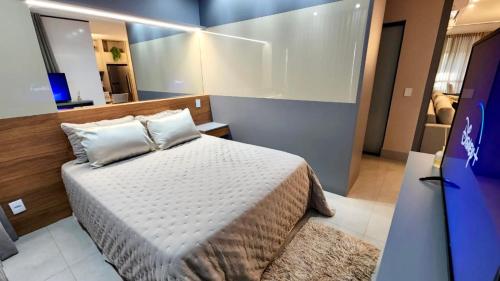 een slaapkamer met een wit bed en een spiegel bij Estúdio Luxuoso no Vertigo com Smart TV na Cama in Campo Grande