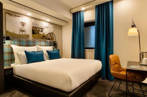 a bedroom with a bed with blue curtains and a desk at Motel One Edinburgh-Royal in Edinburgh