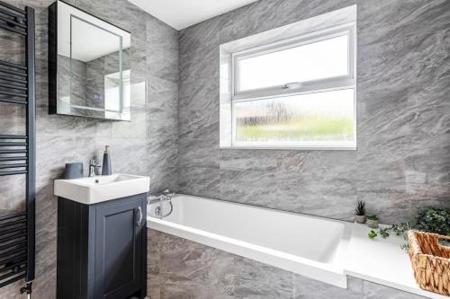 a bathroom with a tub and a sink and a window at Waterside Cottage - Hot Tub, Mooring, Arcade, Bar in Neatishead