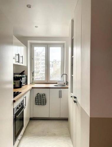 a white kitchen with a sink and a window at Charmant appartement parisien, spacieux & lumineux in Paris