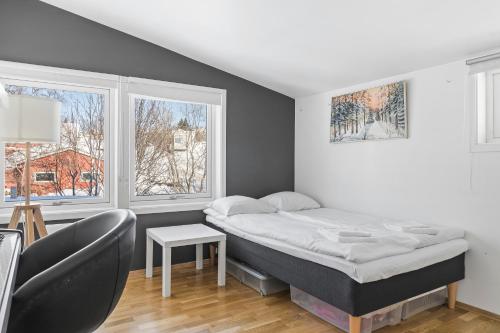 a bedroom with a bed and a chair and two windows at Central Panoramic Retreat in Tromsø