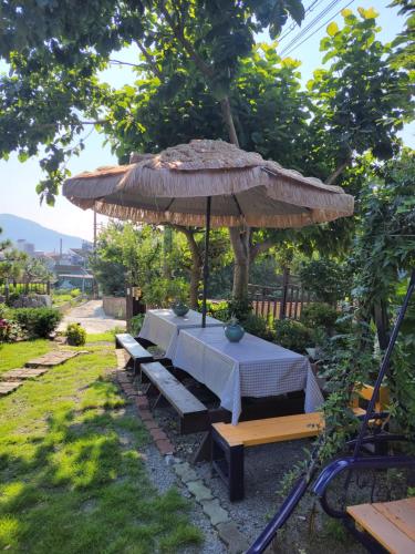 a table with a umbrella and a bench under it at Capri Hakdong Pension in Geoje 