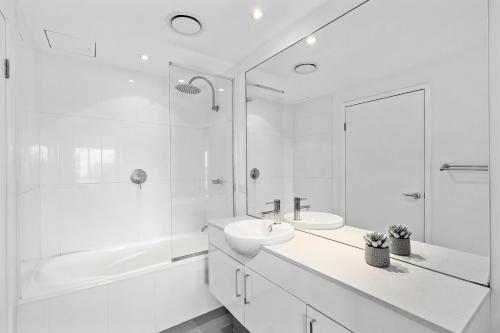 Harbour Quays Apartments في غولد كوست: حمام أبيض مع حوض وحوض استحمام