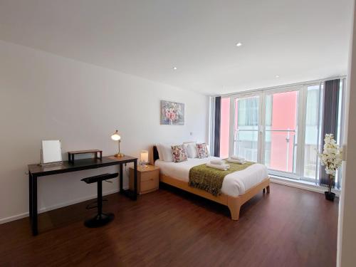 a bedroom with a bed and a desk and windows at Fully Serviced Two Bed Apartment by ExCeL & O2 in London