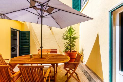 een houten tafel met een parasol op een patio bij Jacuzzi, garden, pool & barbecue beach House, 15mn from Lisbon center in Oeiras