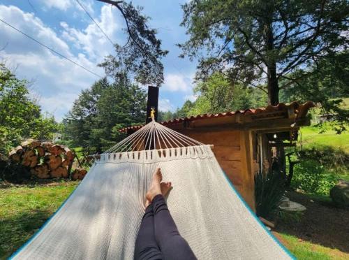 a person laying on a hammock in front of a house at Cabaña del Río in San Pedro Atlapulco