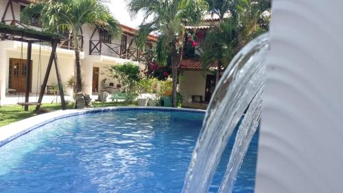 a pool with a water fountain in front of a house at Casa - suites com varanda in Conde