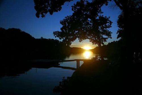 a sunset over a lake with a tree and a bridge at #02 - Unique Lakeside Studio Cottage- Pet Friendly in Hot Springs