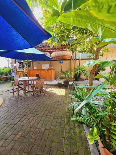un patio con mesa, sillas y sombrilla azul en Ratu Guest House en Kuta