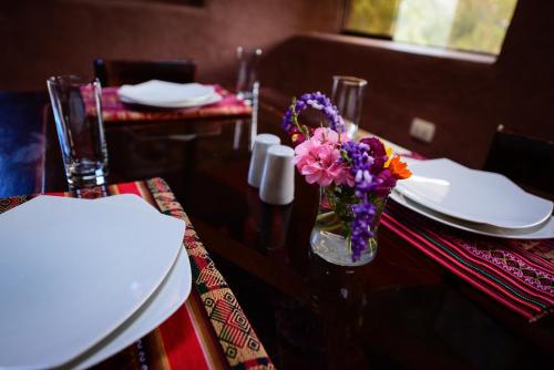 a table with a glass vase with flowers in it at Rumi Lodge Pisac in Pisac