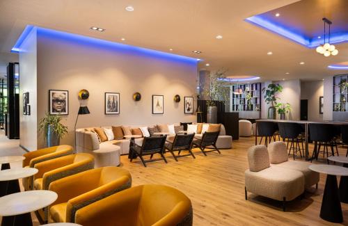 a lobby with chairs and tables and a bar at Leonardo Royal Hotel Cologne Bonn Airport in Cologne