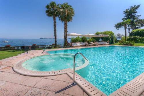 a swimming pool with palm trees and the water at Hotel Villa Capri in Gardone Riviera