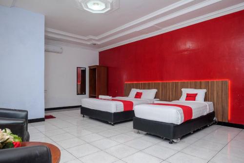 twee bedden in een kamer met een rode muur bij RedDoorz At Pondok Eyang Obi Sleman in Yogyakarta