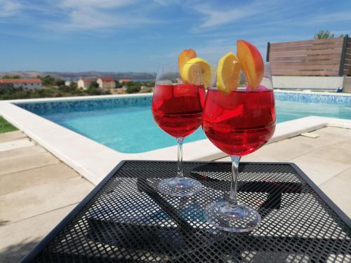 dois copos de vinho sentados numa mesa ao lado de uma piscina em Villa Scolopax rusticola Skradin with heated pool em Skradin