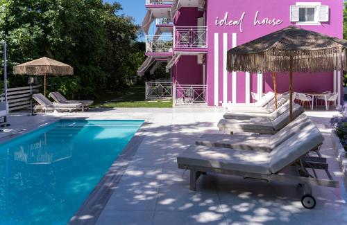 a pool with chairs and an umbrella next to a pink building at Ideal House in Parga