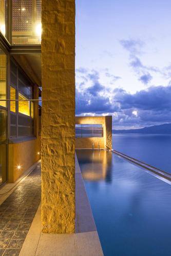 a building with a swimming pool next to the water at Eleni's Serenity - Discovering Sapphire Harmonies in Ravdhoúkha