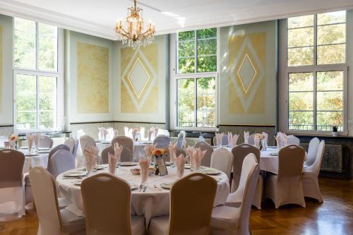 a room with white tables and chairs and windows at Parkhotel Kurhaus in Bad Kreuznach