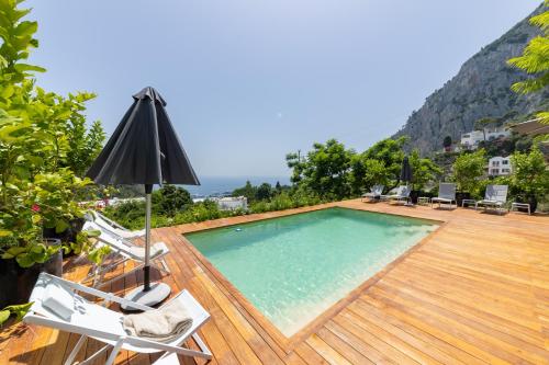a swimming pool on a wooden deck with chairs and an umbrella at Villa La Pergola Capri in Capri