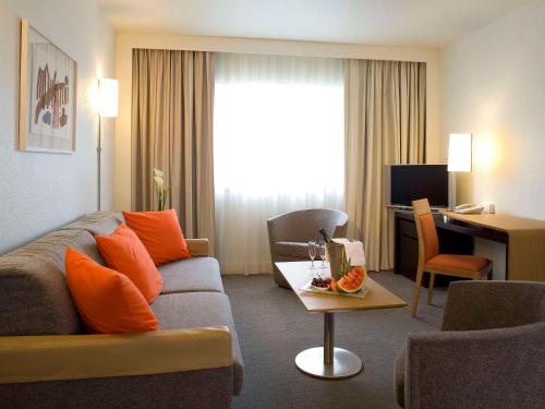 una sala de estar con sofá y escritorio en una habitación de hotel en Novotel Belfort Centre Atria, en Belfort