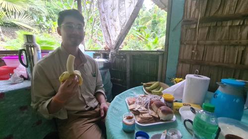 un hombre sentado en una mesa comiendo un plátano en Takapuna Homestay, en Gizo