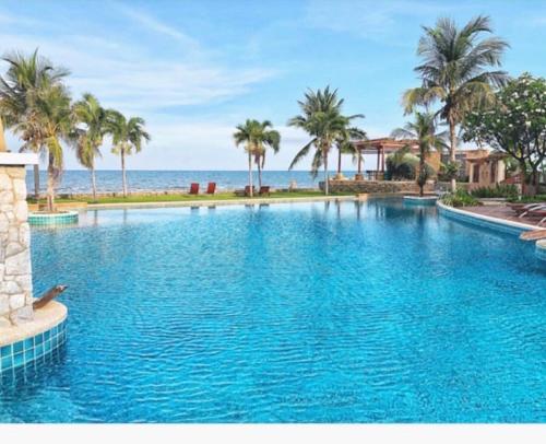 een groot zwembad met palmbomen en de oceaan bij The Seaside One Huahin in Hua Hin