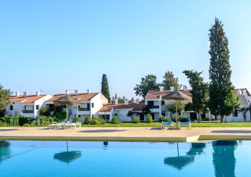a swimming pool with chairs and umbrellas and houses at Pedras Da Rainha in Cabanas de Tavira