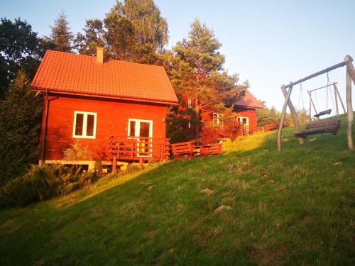 a small red house on a hill with a swing at BieszczadzkaDolina in Zagórz