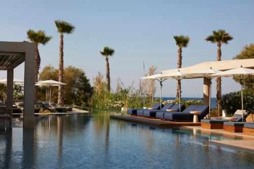a pool with chairs and umbrellas and palm trees at Avant Mar Paros in Naousa