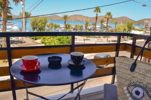 a table with two cups on a balcony with a view of the beach at Boho Sea View Apartment in Elounda