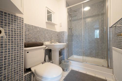La salle de bains est pourvue de toilettes, d'un lavabo et d'une douche. dans l'établissement Bright and modern 4-bed townhouse with garden near town centre, à Kent