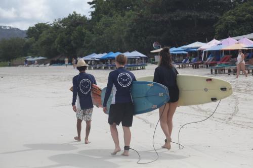 three people walking on the beach with their surfboards at Roby Homestay in Kuta Lombok
