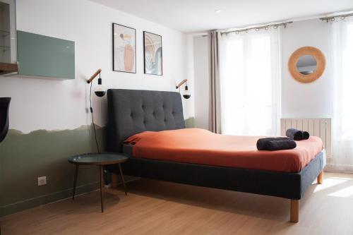 a bedroom with a bed with orange sheets and a table at Studio cosy en plein cœur historique de Pontoise in Pontoise
