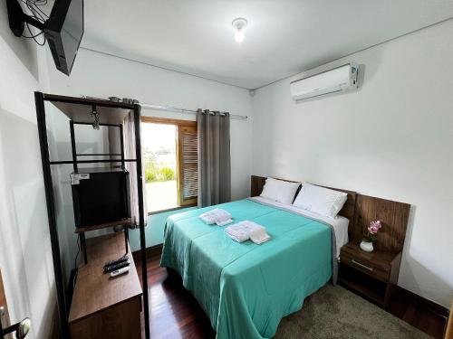 a bedroom with a bed with a green blanket and a television at Pousada Ouro Verde in São Roque