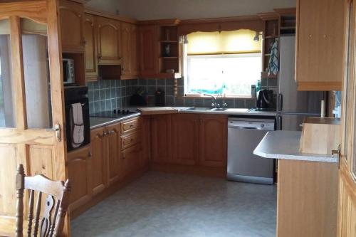 a kitchen with wooden cabinets and a sink and a window at Three Sisters Holiday Home - 7km to Dingle in Ballyferriter