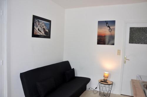 sala de estar con sofá negro y cuadros en la pared en AU BORD DE L'EAU studio 1, en Chambon-sur-Voueize