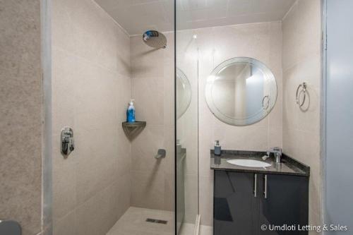 a bathroom with a shower with a sink and a mirror at COZUMEL 213 in Umdloti