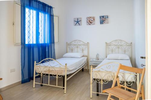 twee bedden in een kamer met blauwe gordijnen en een raam bij Nicolò House 1 in Torre San Giovanni Ugento