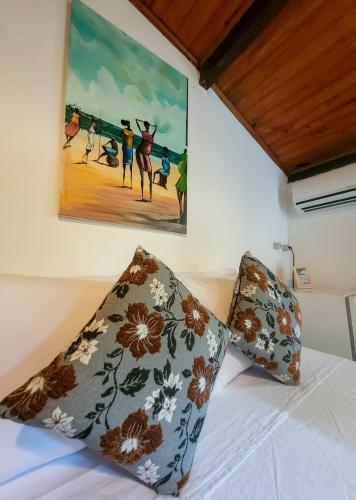 a bed with two pillows and a painting on the wall at Pousada Raiz Forte in Caraíva